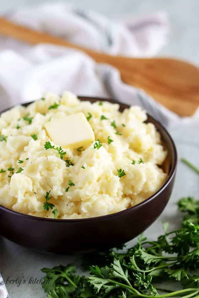 Final shot of the garlic mashed potatoes in a bowl, with butter and parsley.
