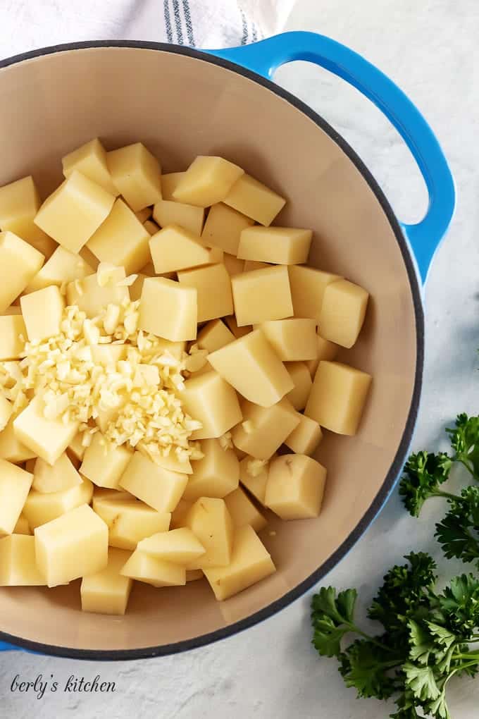 The dutch oven loaded with raw cubed potatoes and chopped raw garlic.