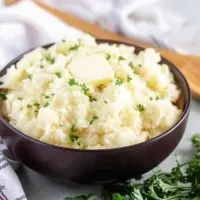 Garlic mashed potatoes in a brown bowl, topped with unsalted butter.