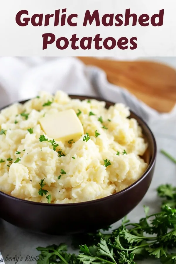 A bowl of garlic mashed potatoes, garnished with parsley and unsalted butter.
