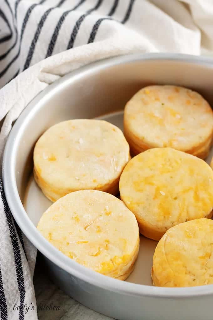 Raw cheddar biscuits have been placed in a cake pan for baking.
