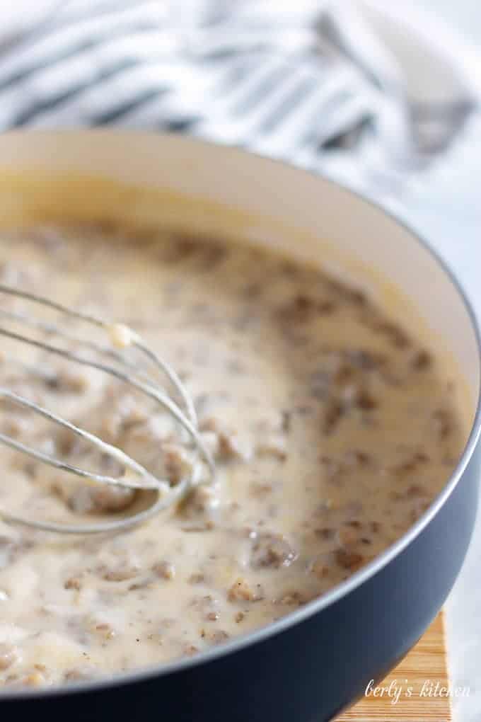 Stirring the sausage gravy, with a whisk, as it thickens.