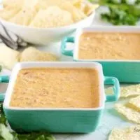 Two square bowls of seasoned beef queso dip with tortilla chips.
