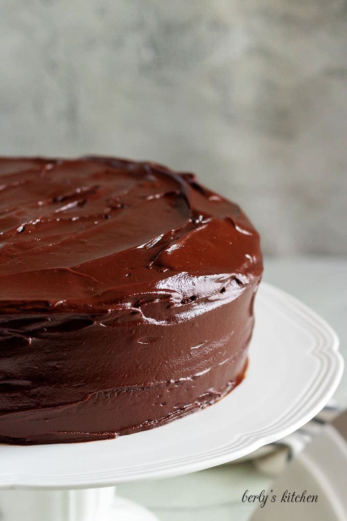 The cake has been placed on a stand and covered in ganache.