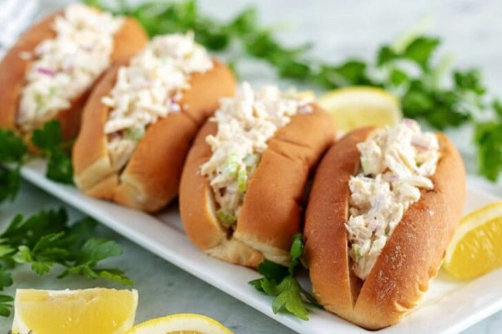 Four crab rolls, on a long rectangular plate, garnished with fresh parsley.