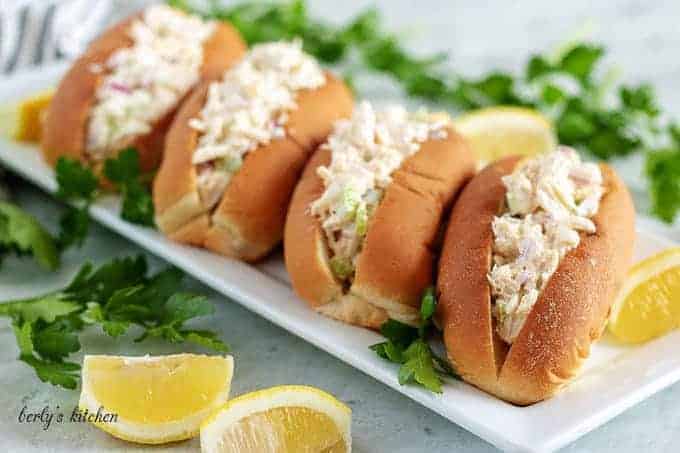 Four crab rolls, on a long rectangular plate, garnished with fresh parsley.