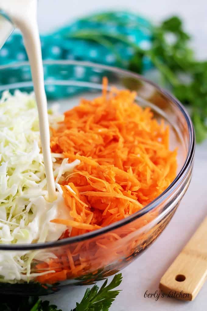 The coleslaw dressing being poured over the cabbage and carrots.