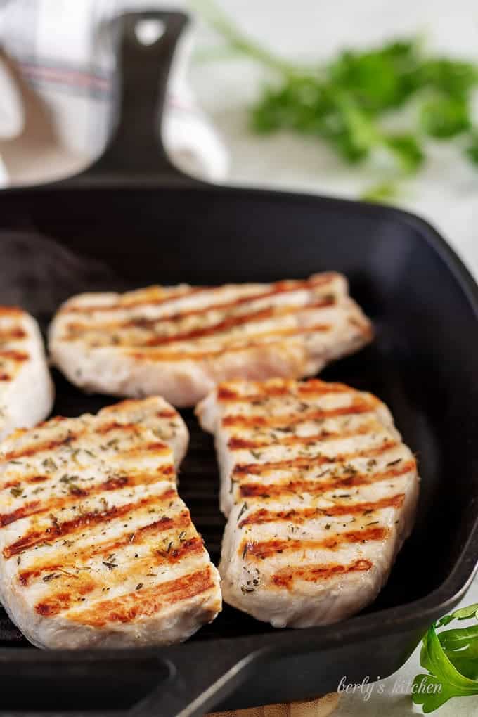 Four cast iron pork chops grilling in a cast iron griddle pan.