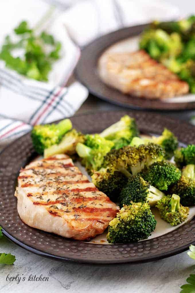 Two plates of grilled pork chops served with the broccoli.