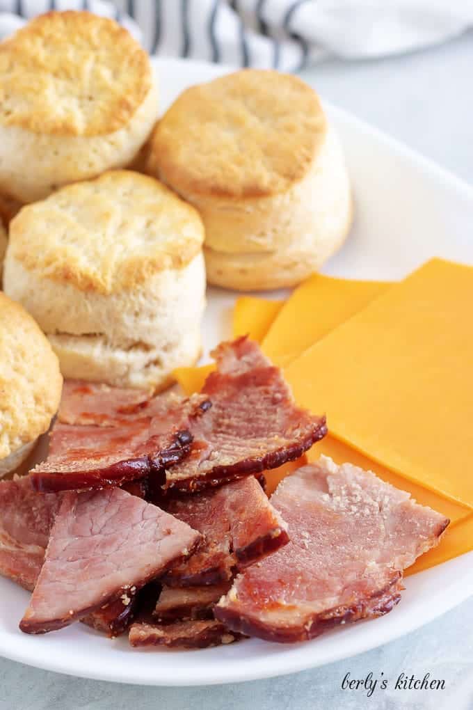 Homemade biscuits, pan seared ham, and cheddar cheese on a plate.