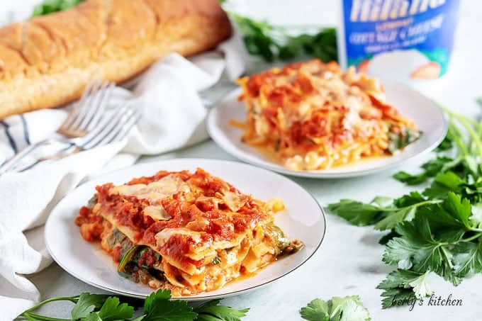 Two pieces of mushroom lasagna on with plates garnished with parsley.