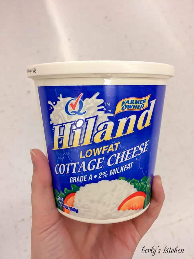 My hand holding a package of Hiland Dairy low fat cottage cheese.