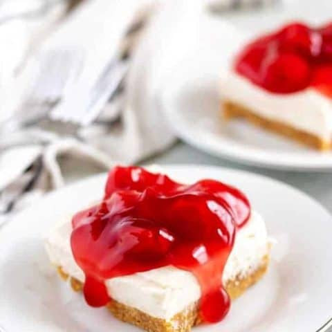 Two cheesecake bars, on white plates, covered with cherry topping.