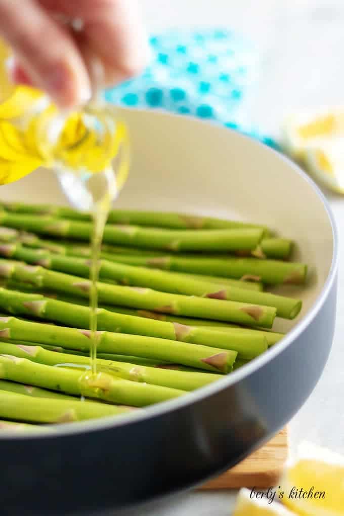 Olive oil being poured over asparagus, in the saute pan.