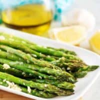 Finished asparagus, covered in garlic, served on a rectangular plate.