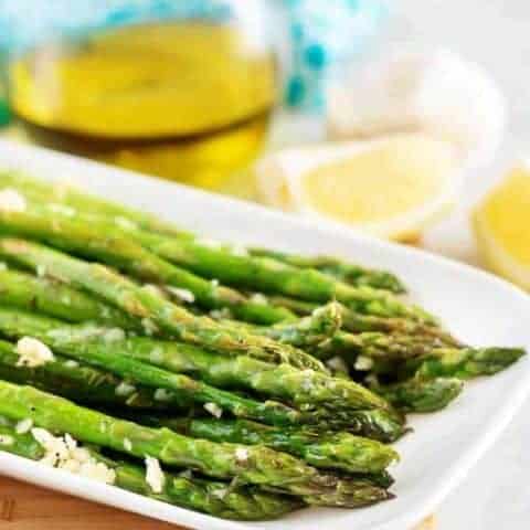 Finished asparagus, covered in garlic, served on a rectangular plate.