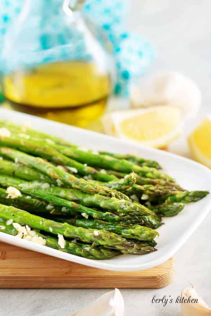 Finished asparagus, covered in garlic, served on a rectangular plate.