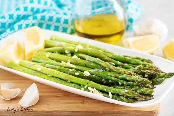 The sauteed asparagus, topped with garlic, sitting on a rectangular plate.