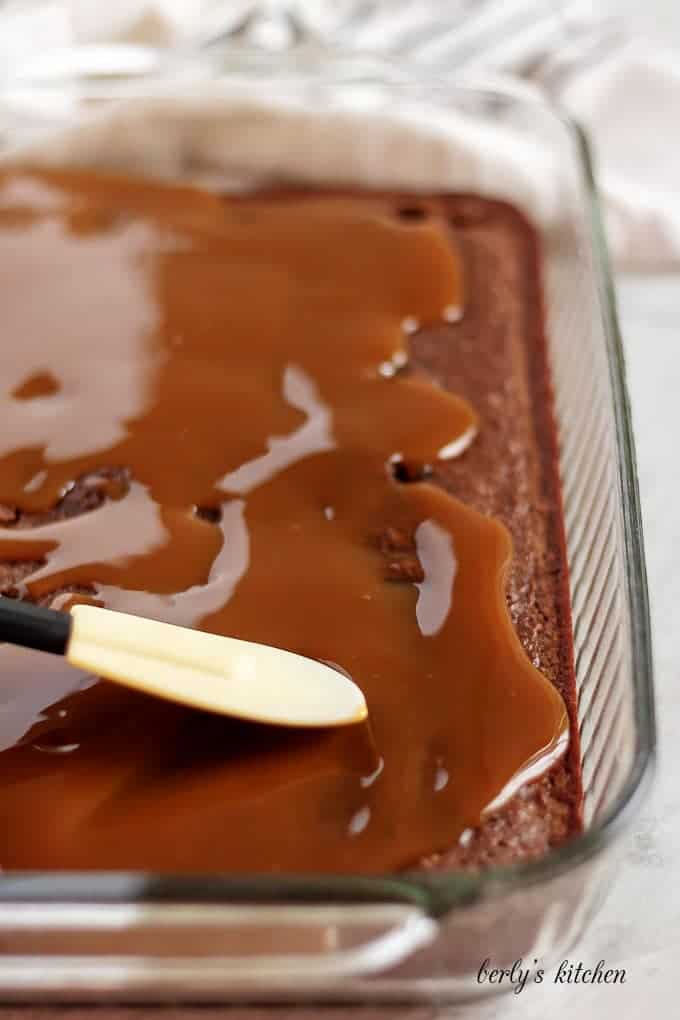 Using a spatula to evenly spread the caramel sauce over the brownies.