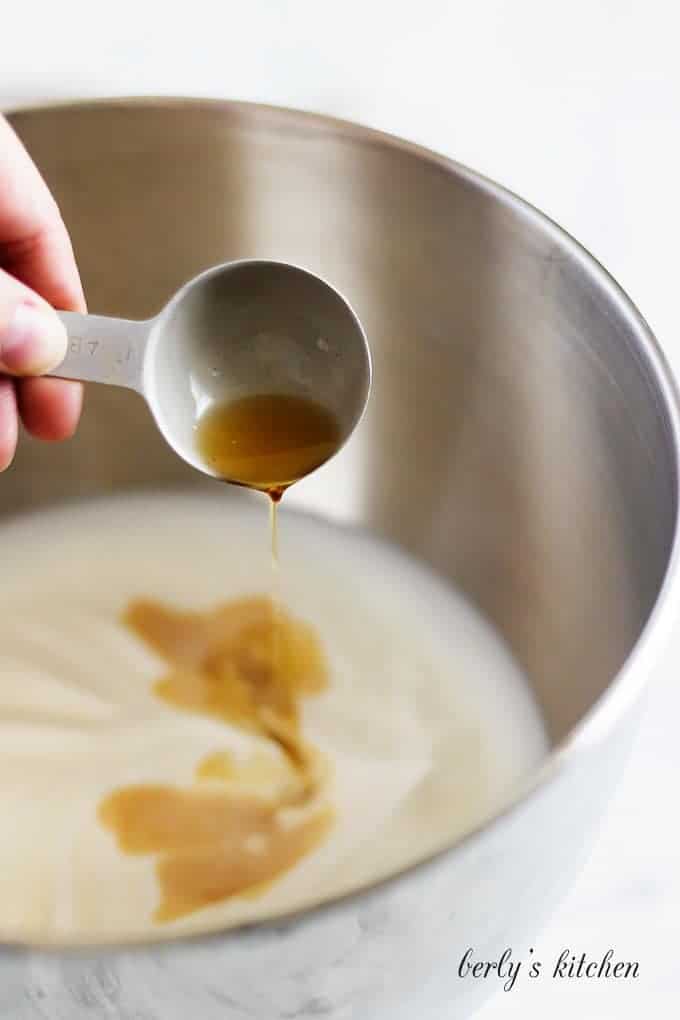 The amaretto being added to the mixing bowl filled with heavy cream.