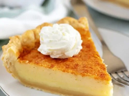 A large piece of buttermilk pie topped with whipped cream.