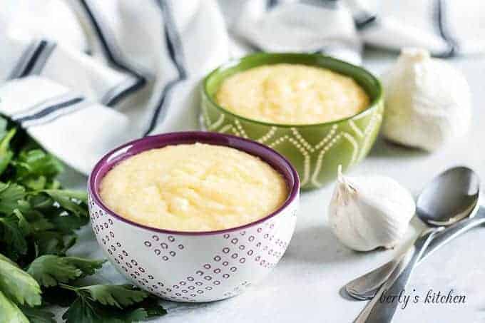 Two, colorful bowls, filled with cheese grits, and staged with garlic.