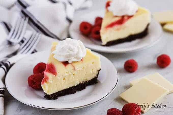 Slices of instant pot white chocolate raspberry cheesecake on white plates.