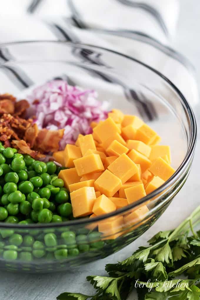 The peas, cheese, bacon, and red onions in a mixing bowl.