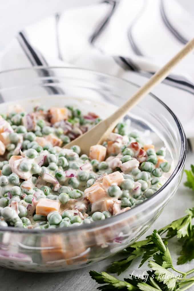 The pea salad has been mixed using a wooden spoon.