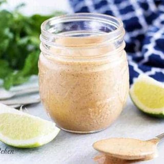 The creamy Southwest dressing in a small mason jar, surrounded by limes.