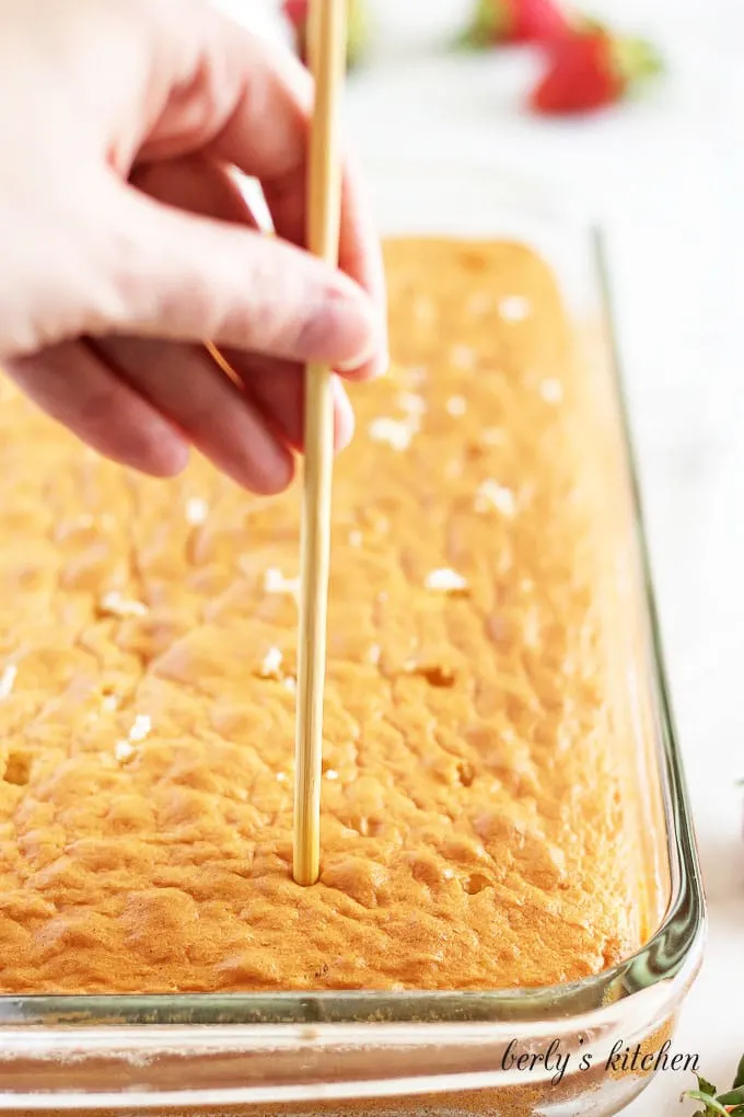 The sheet cake is done and being poked with a wooden spoon.