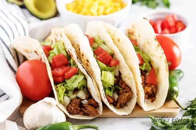 Three turkey tacos topped with shredded lettuce and diced tomatoes.