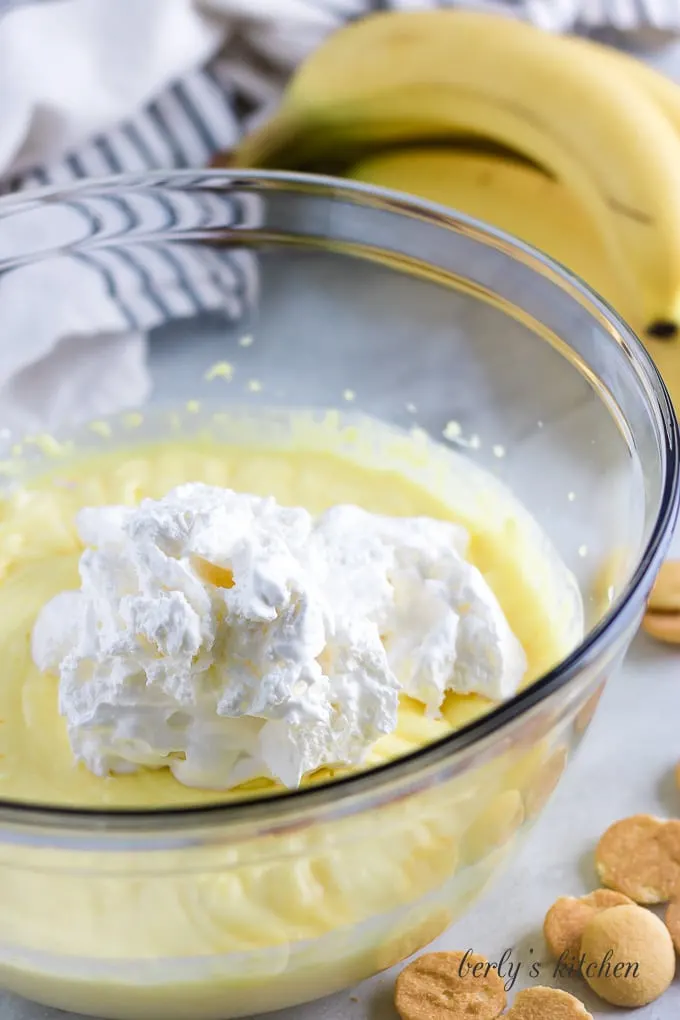 Pudding and whipped topping in a large glass mixing bowl.