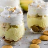 Two mini mason jars filled with banana pudding topped with whipped cream.