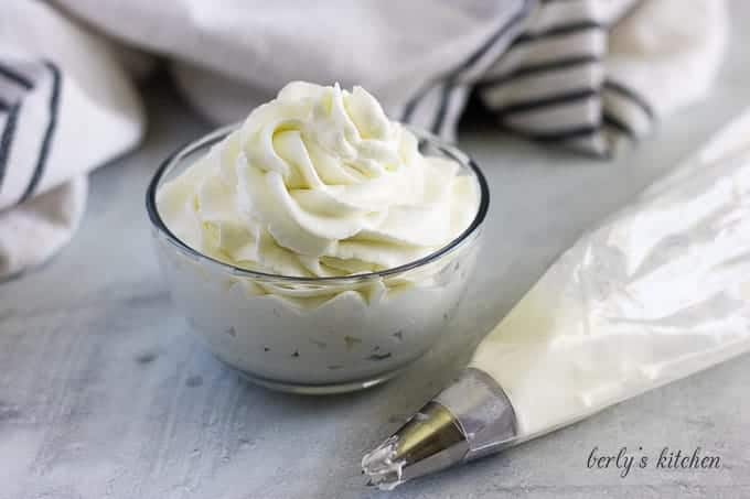 A bowl of homemade whipped cream sitting next to a piping bag.