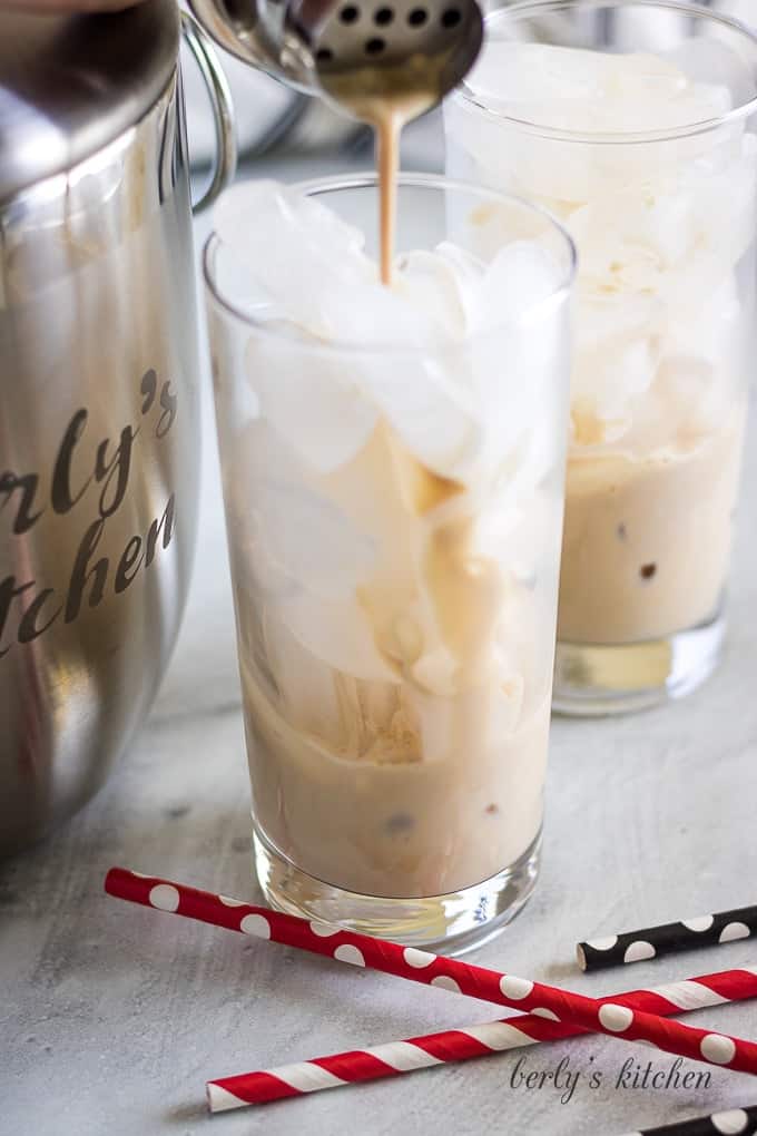 The irish cream being poured into a glass filled with ice.