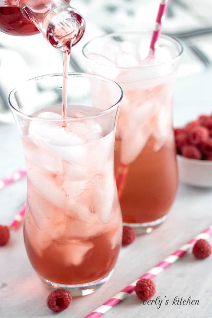 Raspberry syrup being poured into a glass with club soda and ice.