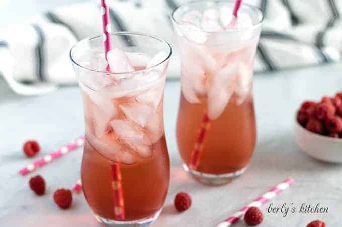 Two glasses of raspberry Italian soda served with ice and straws.