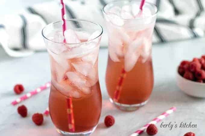 Two glasses of raspberry italian soda served with ice and straws.