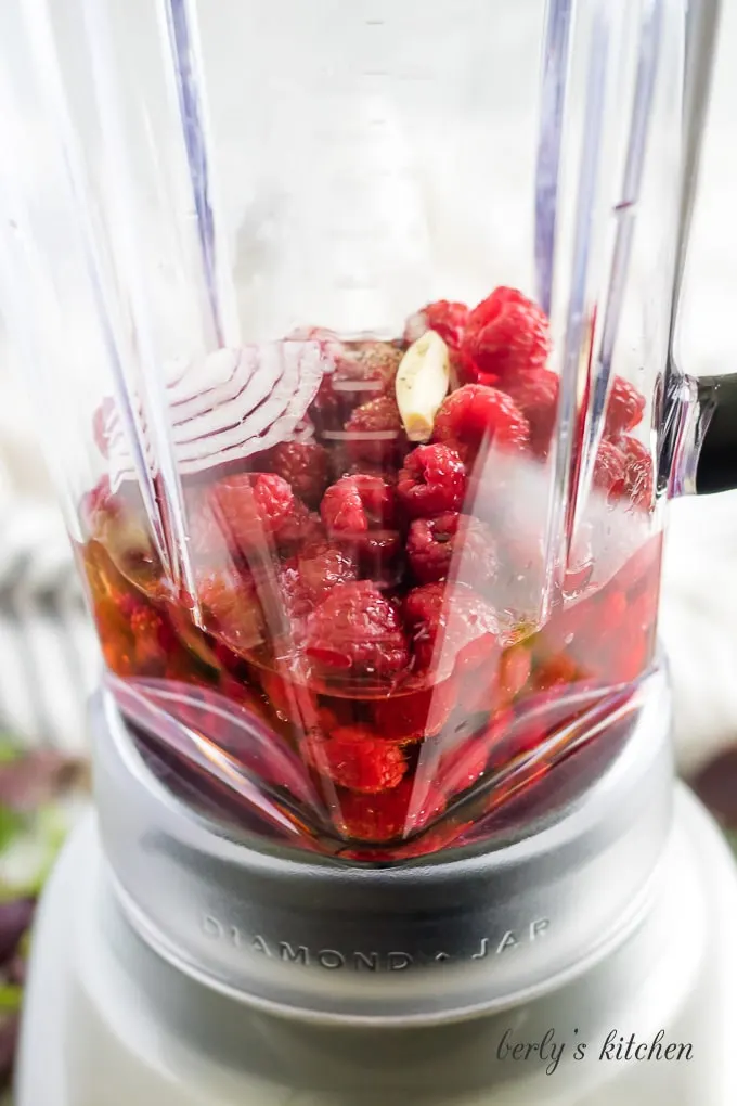 Raspberries, olive oil, and other ingredients in a blender to be combined.