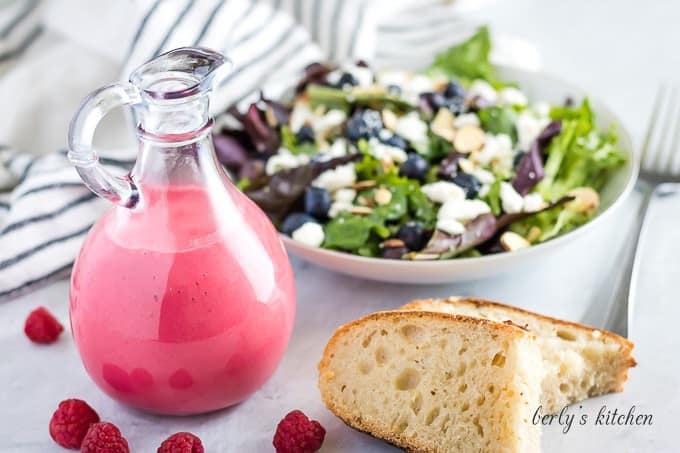The finished raspberry vinaigrette in a bottle served with salad and bread.