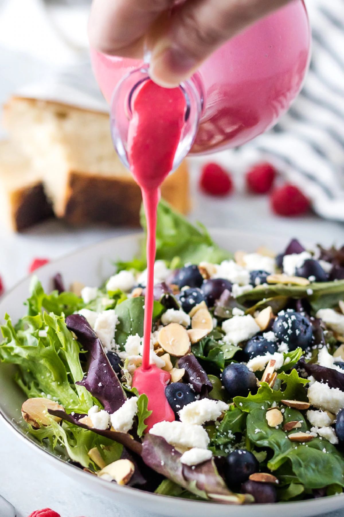 The raspberry vinaigrette being drizzled over a fresh Spring mix salad.