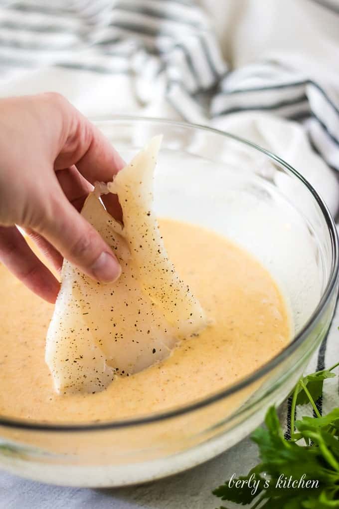 A piece of cod being dipped into the beer batter.