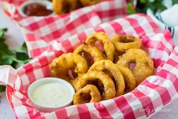 A serving of beer battered onion rings, in a basket, with ranch.