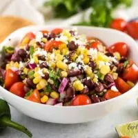 A bowl filled with corn and black bean salsa garnished with limes.