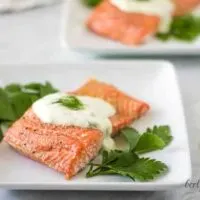 The finished baked salmon topped with dill sauce and garnished with parsley.