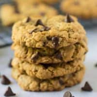 Four stacked oatmeal chocolate chip cookies surrounded by chocolate chips.