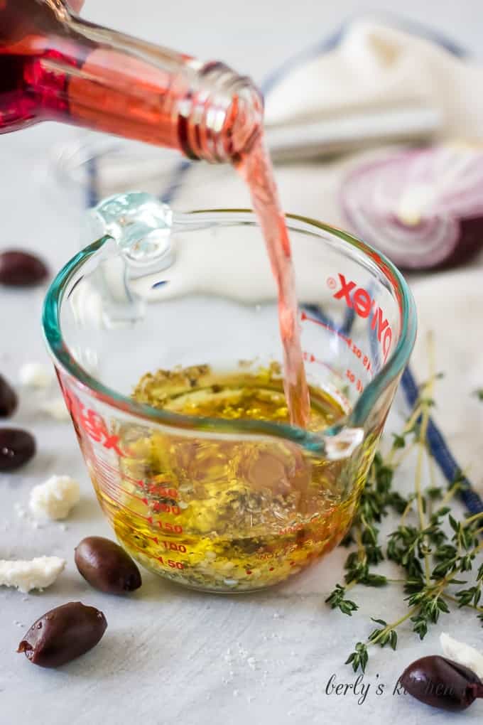 Red wine vinegar being poured into a measure cup with oil.