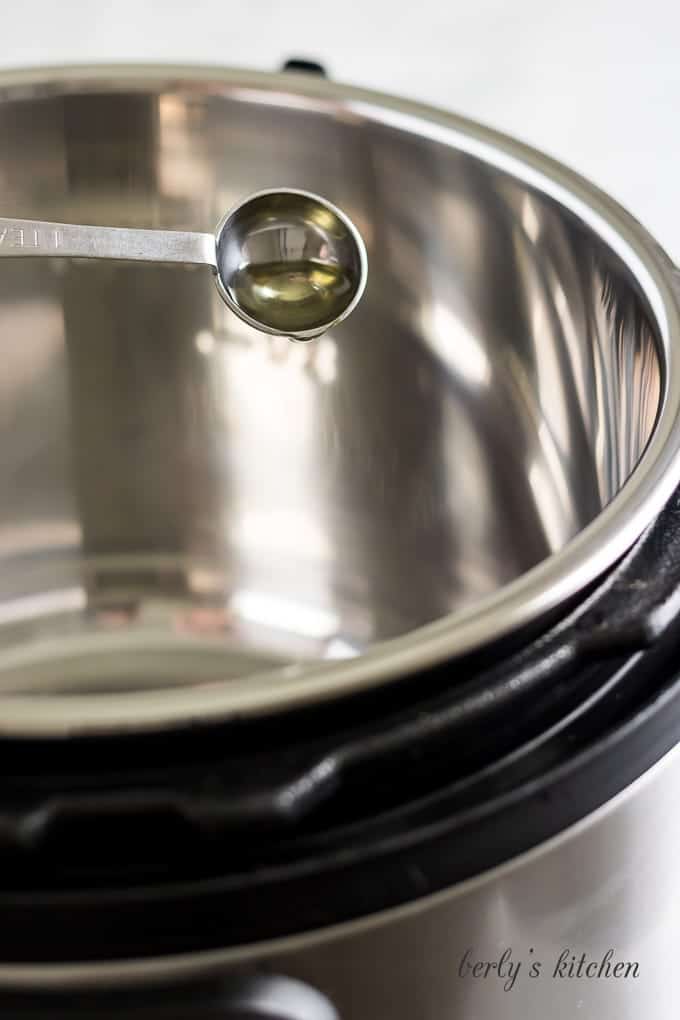 Teaspoon of olive oil being poured into the instant pot.