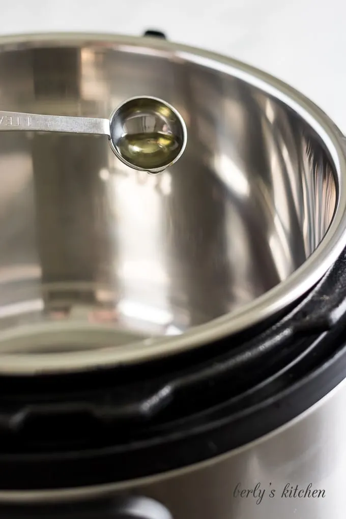 Teaspoon of olive oil being poured into the Instant Pot.